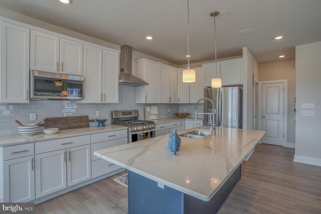 kitchen with tasteful backsplash, wall chimney range hood, sink, a center island with sink, and appliances with stainless steel finishes