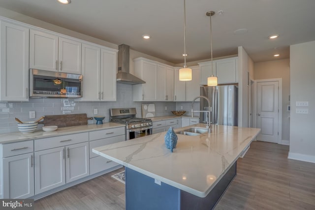 kitchen with a sink, appliances with stainless steel finishes, wall chimney exhaust hood, and a kitchen island with sink