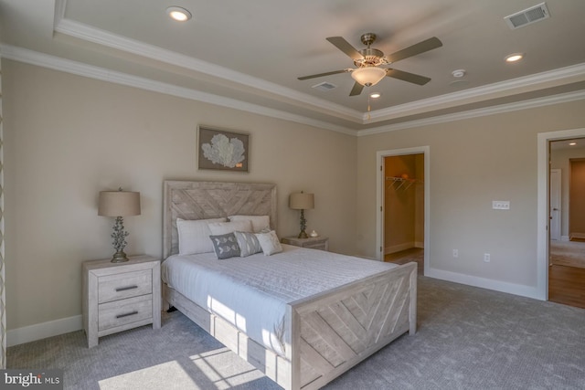 carpeted bedroom featuring crown molding, ceiling fan, a walk in closet, a raised ceiling, and a closet