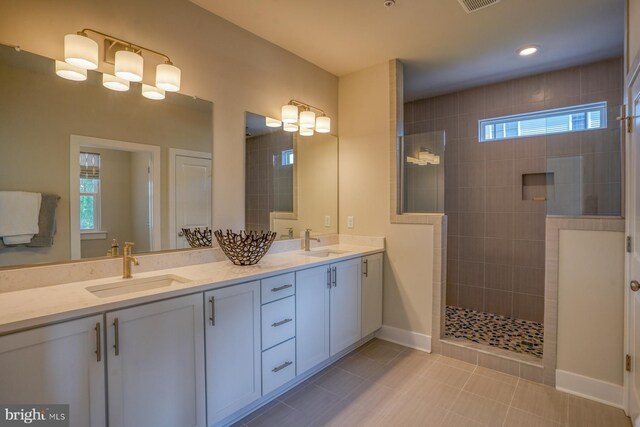 bathroom with tiled shower, tile patterned floors, a wealth of natural light, and dual bowl vanity