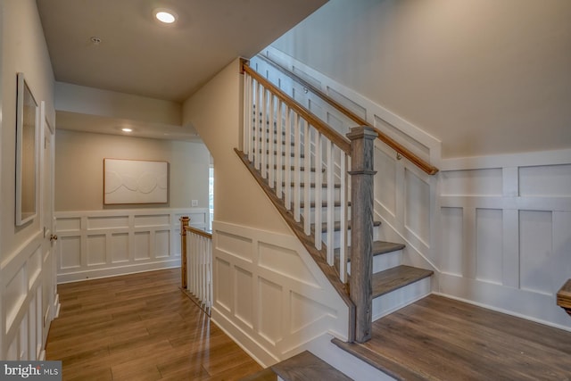 stairway with recessed lighting, a decorative wall, and wood finished floors