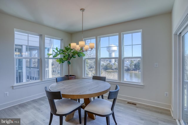 dining area with light wood-type flooring, visible vents, a chandelier, and baseboards