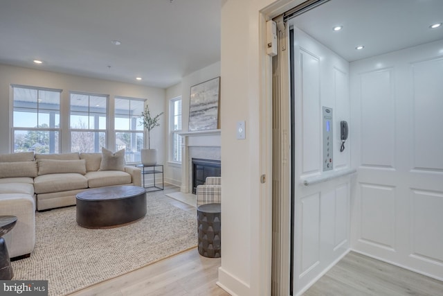 living room featuring recessed lighting, light wood-style floors, and a fireplace with flush hearth