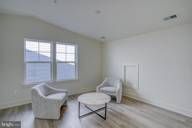 living area with visible vents, baseboards, vaulted ceiling, and light wood-type flooring