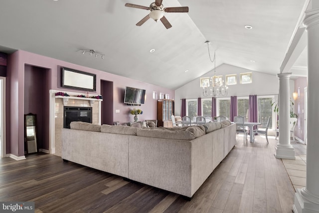 living room with dark wood-style floors, a tiled fireplace, high vaulted ceiling, ornate columns, and ceiling fan with notable chandelier