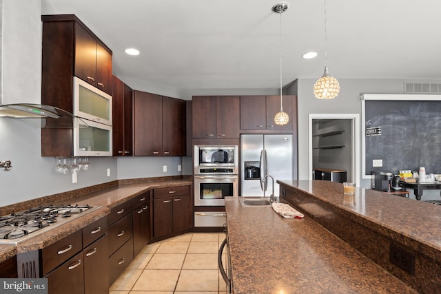 kitchen with decorative light fixtures, dark brown cabinets, appliances with stainless steel finishes, sink, and wall chimney range hood