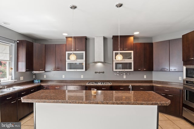 kitchen with pendant lighting, appliances with stainless steel finishes, wall chimney range hood, and dark stone counters