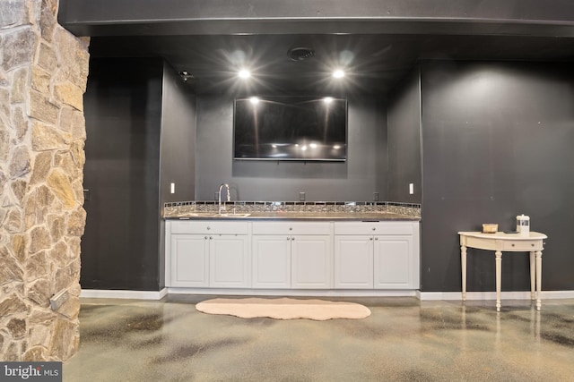 bar with dark stone counters, sink, and white cabinetry