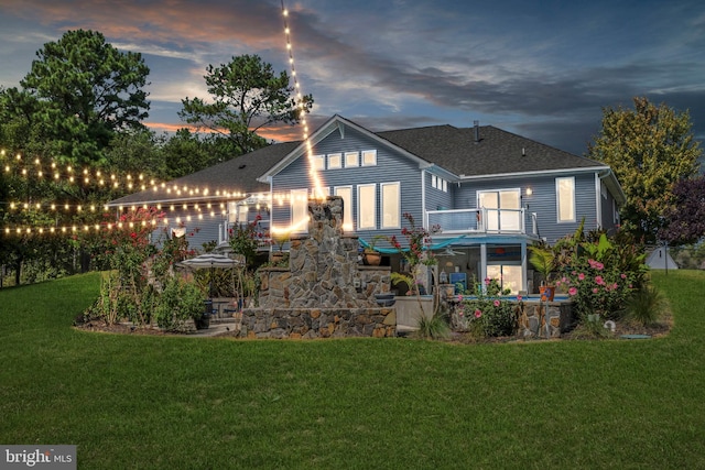 back house at dusk featuring a balcony and a yard