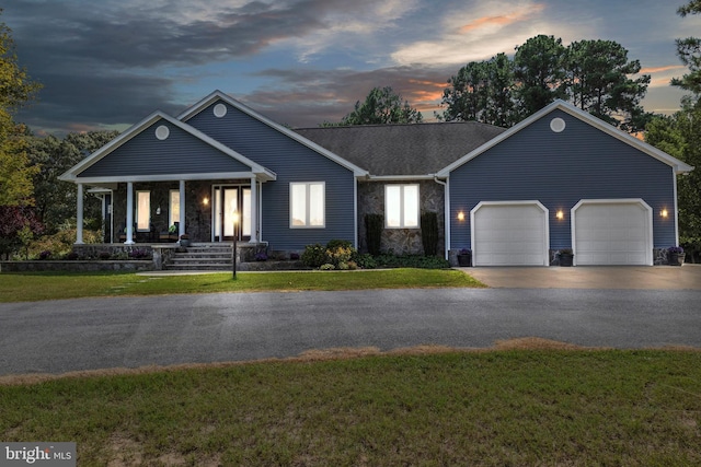 view of front of property with covered porch, a lawn, and a garage