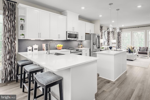 kitchen featuring white cabinetry, appliances with stainless steel finishes, light hardwood / wood-style floors, decorative light fixtures, and backsplash