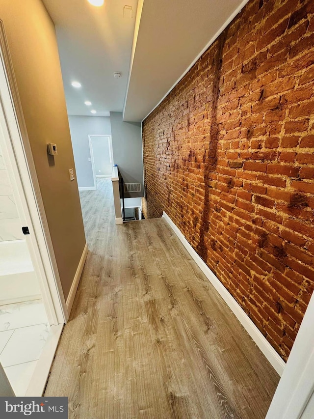 corridor with brick wall and wood-type flooring