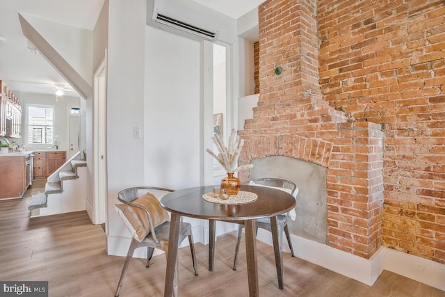 dining area with brick wall, a brick fireplace, ceiling fan, light hardwood / wood-style flooring, and a wall unit AC