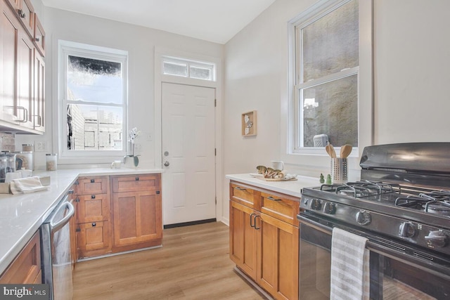 kitchen with black gas stove, stainless steel dishwasher, light wood-type flooring, and vaulted ceiling