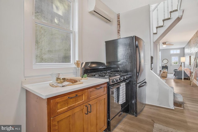 kitchen with light hardwood / wood-style flooring, ceiling fan, black range with gas cooktop, and a wall mounted AC