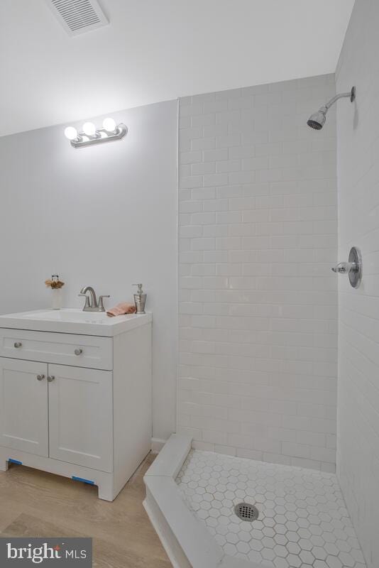 bathroom with wood-type flooring, vanity, and tiled shower