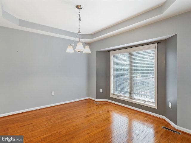 spare room with a tray ceiling, a chandelier, and hardwood / wood-style flooring