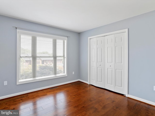 unfurnished bedroom featuring multiple windows, a closet, and dark hardwood / wood-style flooring