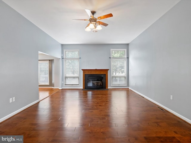 unfurnished living room featuring a wealth of natural light, dark wood-type flooring, and ceiling fan