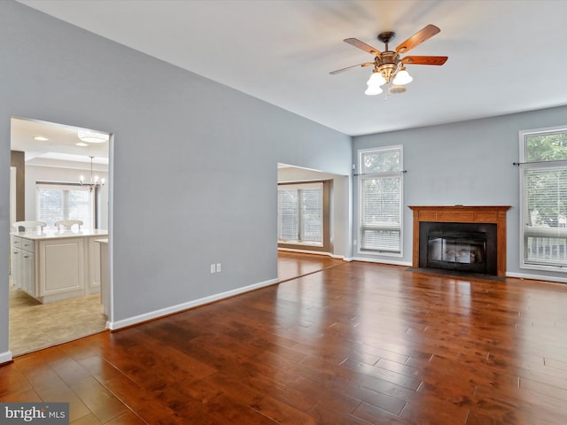 unfurnished living room with ceiling fan with notable chandelier, a wealth of natural light, and dark hardwood / wood-style flooring