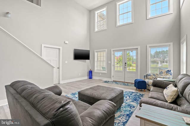 living room featuring a high ceiling, light hardwood / wood-style flooring, and french doors