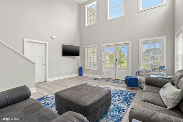 living room featuring a towering ceiling, light hardwood / wood-style flooring, and french doors