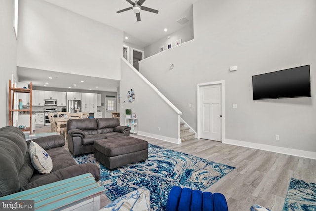 living room with ceiling fan, light hardwood / wood-style flooring, and a towering ceiling