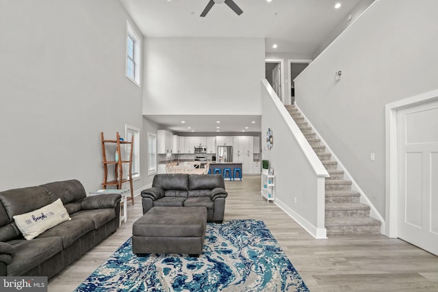 living room with light hardwood / wood-style flooring, ceiling fan, and a high ceiling