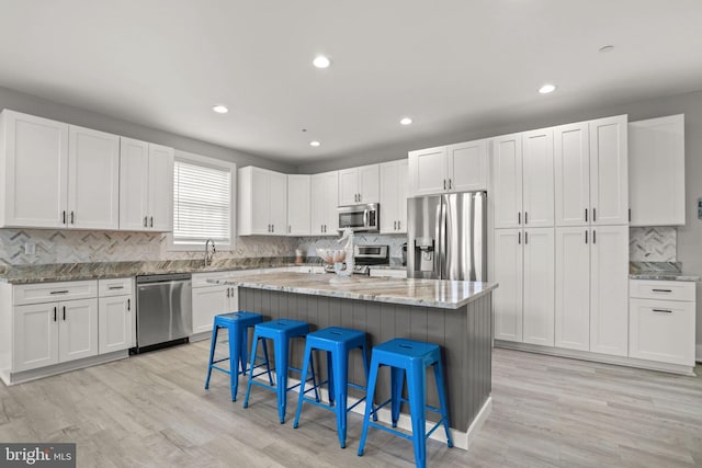 kitchen featuring appliances with stainless steel finishes, white cabinetry, a kitchen breakfast bar, a center island, and light stone countertops