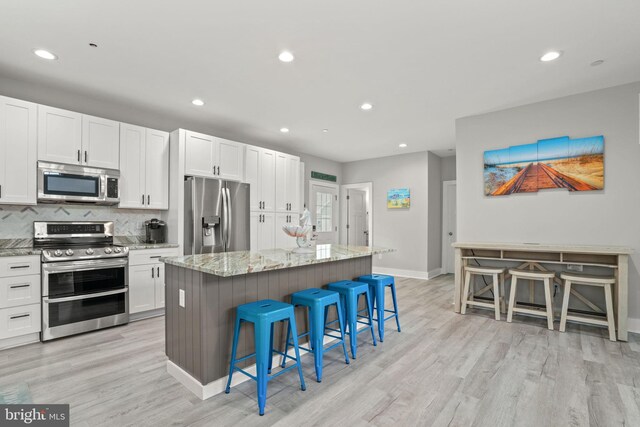 kitchen with a kitchen island, appliances with stainless steel finishes, a breakfast bar, white cabinetry, and light stone counters