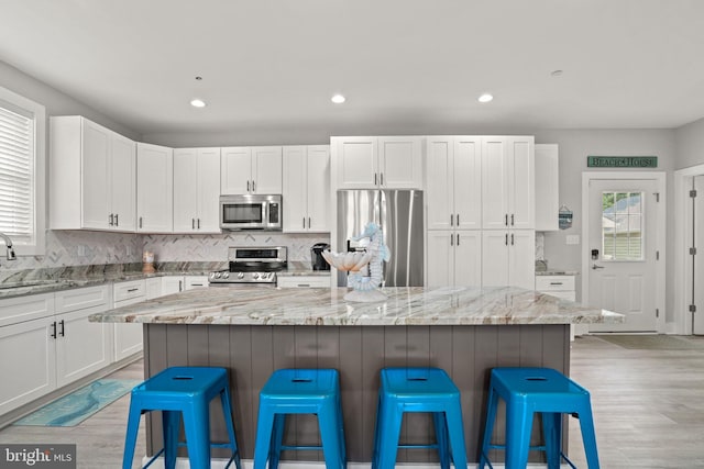 kitchen with light stone countertops, stainless steel appliances, a breakfast bar, and a kitchen island