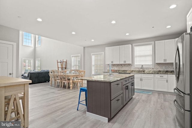 kitchen featuring white cabinetry, light stone counters, a center island, stainless steel refrigerator, and gray cabinets