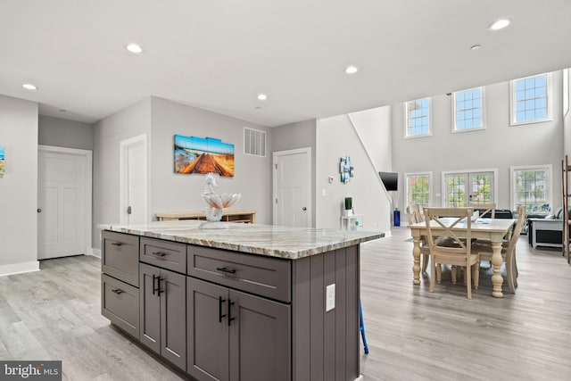 kitchen featuring gray cabinets, a center island, light stone counters, light hardwood / wood-style floors, and french doors