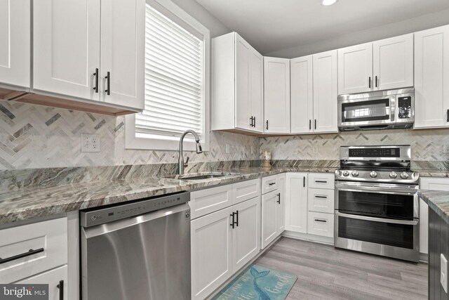 kitchen with sink, light stone counters, white cabinets, stainless steel appliances, and backsplash