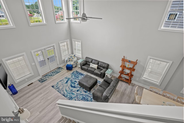 living room with a towering ceiling, light hardwood / wood-style floors, french doors, and ceiling fan