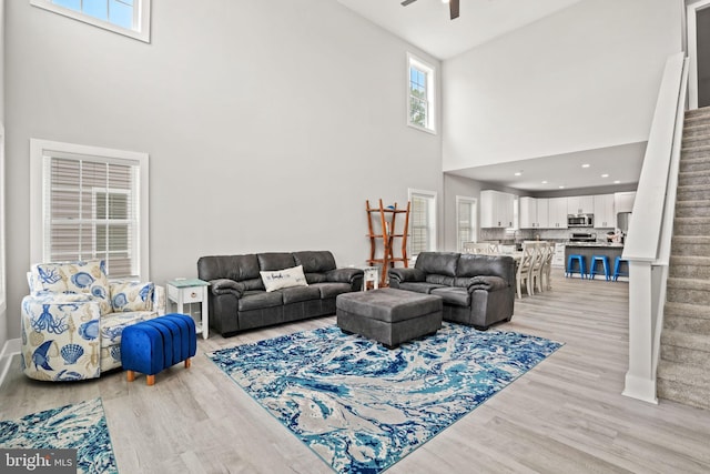 living room featuring a high ceiling, ceiling fan, and light wood-type flooring