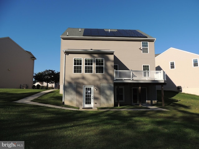 rear view of property with a deck, a lawn, and solar panels