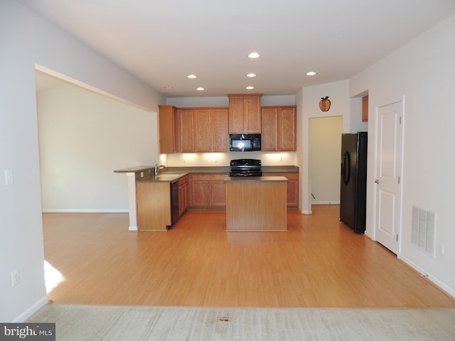 kitchen featuring sink, light wood-type flooring, a kitchen island, and black appliances