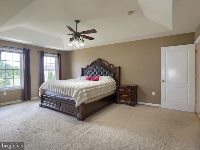 carpeted bedroom with ceiling fan and a raised ceiling