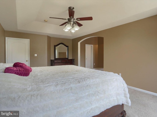 bedroom with a raised ceiling, carpet, and ceiling fan