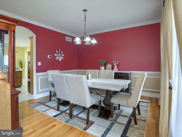 dining area with a chandelier, light wood-type flooring, and ornamental molding