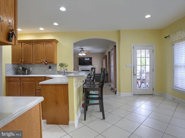 kitchen with a kitchen bar, sink, backsplash, light tile patterned floors, and ceiling fan