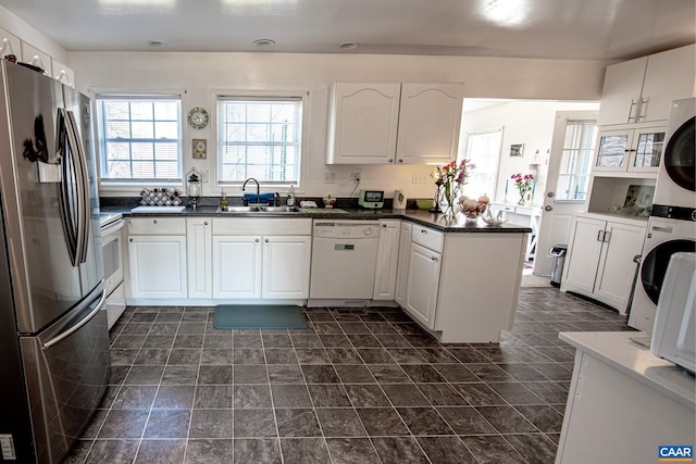 kitchen with white cabinetry, white appliances, sink, and stacked washer and dryer