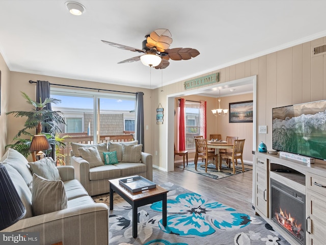 living room with crown molding, ceiling fan with notable chandelier, and wood-type flooring