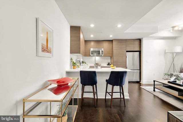 kitchen featuring a kitchen bar, stainless steel appliances, kitchen peninsula, backsplash, and dark hardwood / wood-style floors