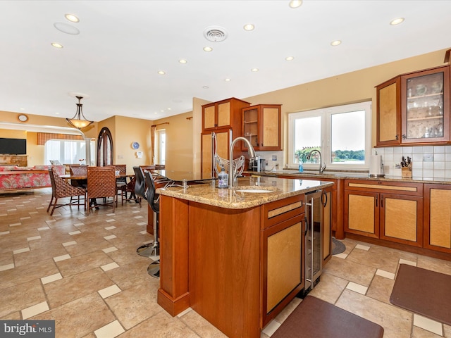 kitchen with sink, light stone counters, a wealth of natural light, a center island with sink, and beverage cooler