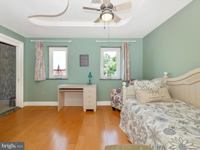 bedroom with ceiling fan, light wood-type flooring, and a tray ceiling