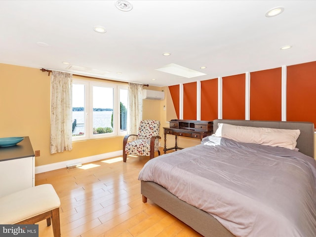 bedroom featuring a skylight, light hardwood / wood-style flooring, a wall mounted AC, and a water view