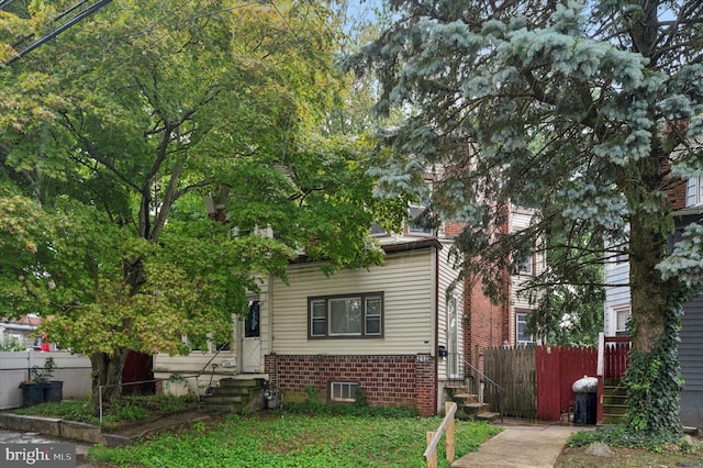 view of property hidden behind natural elements featuring brick siding and fence