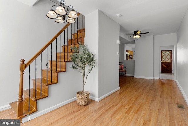 stairs featuring ceiling fan with notable chandelier and hardwood / wood-style flooring